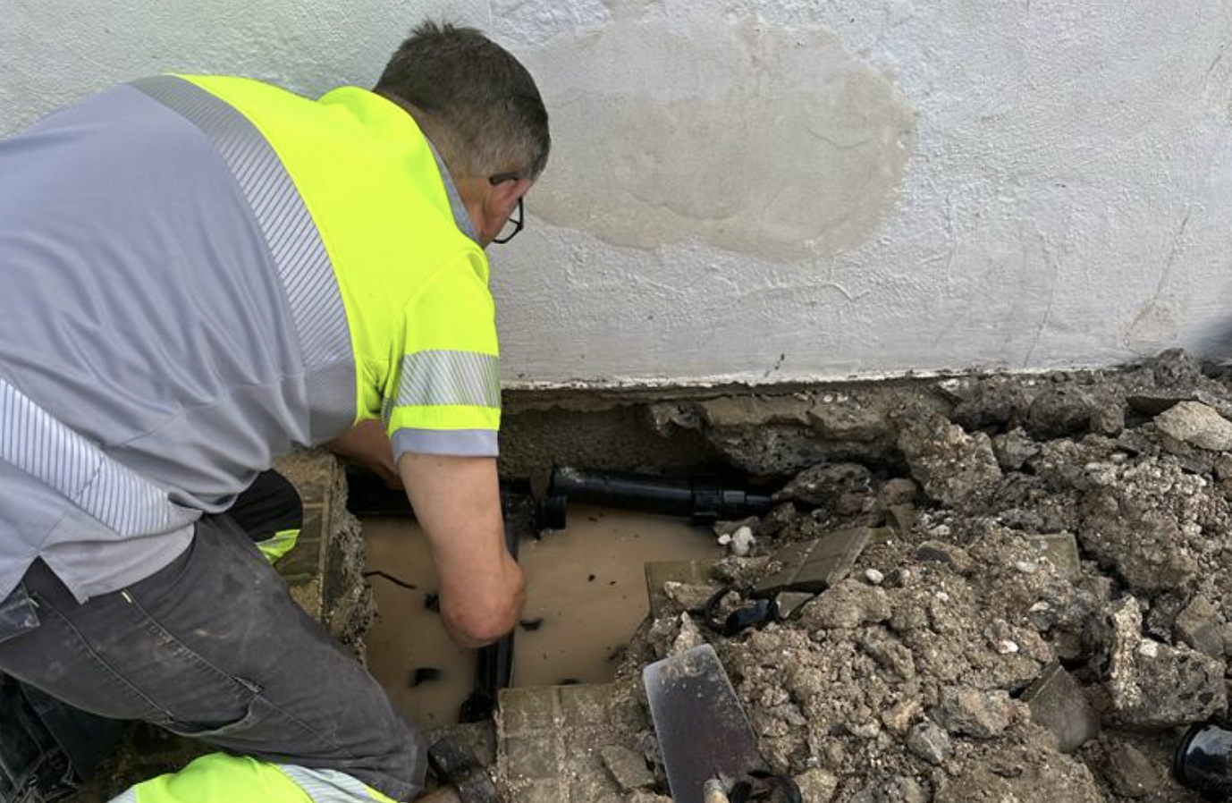Un operario de Aguas de Lucena arregla la avería en la red junto al muro del edificio