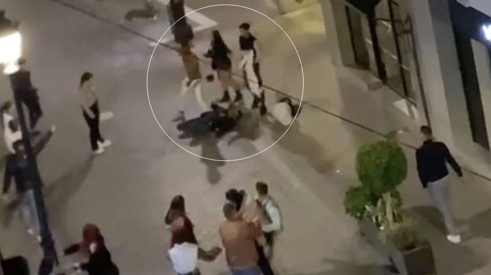  Fotograma del vídeo difundido en redes sociales que recoge parte de la pelea en la calle el Peso. Un joven con pantalón blanco golpea a otro hombre, tendido en el suelo, mientras la escena es observada por varias personas. 