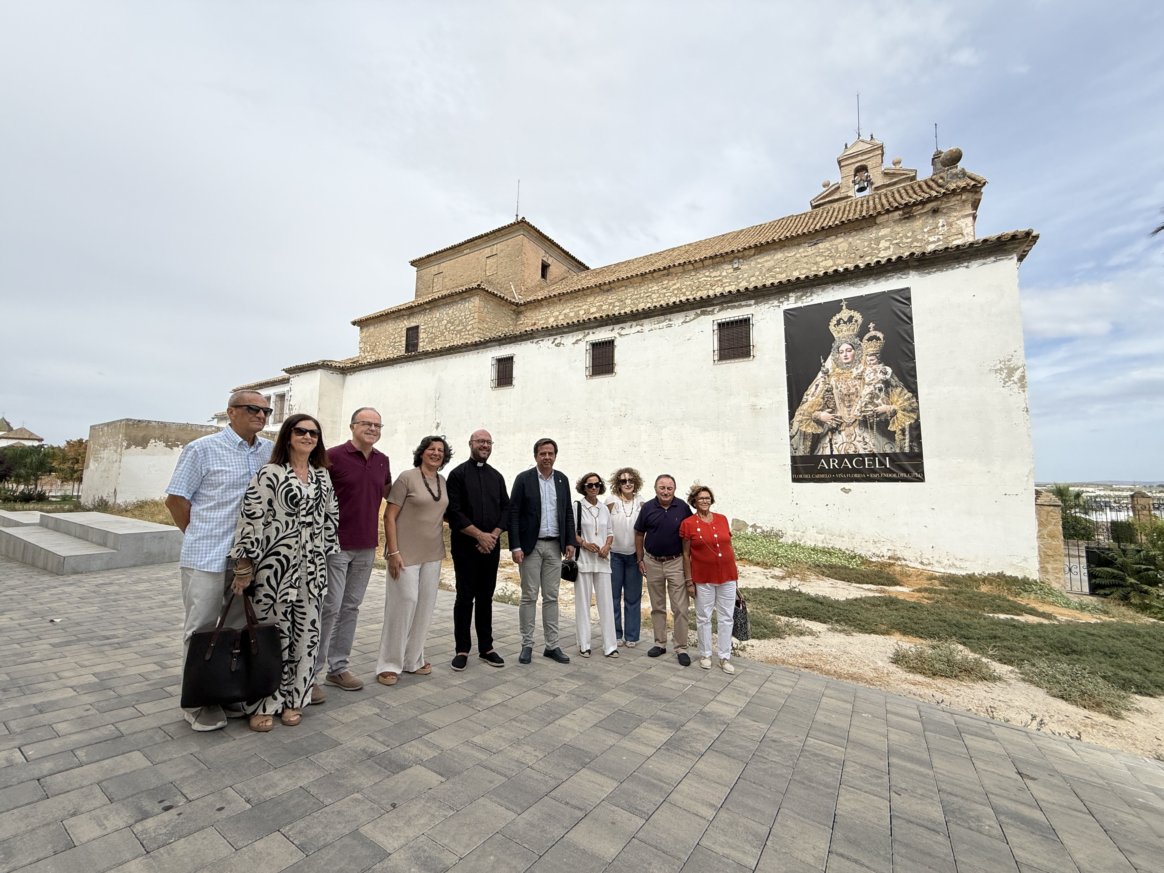 El alcalde de Lucena, Aurelio Fernández, junto al párroco del Carmen, Eugenio Bujalance, voluntarios e integrantes de Cáritas, ante el terreno cedido para la construcción del nuevo centro de atención y almacén.